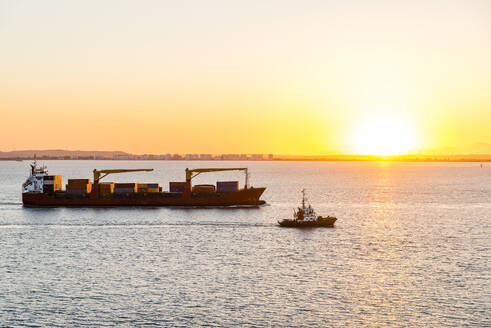 Spanien, Andalusien, Cadiz, Boot fährt an fahrendem Containerschiff bei Sonnenuntergang vorbei - EGBF00939