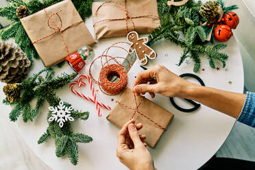 Overhead von gesichtslosen unerkennbaren Person schmücken Geschenk-Box mit Band auf, während Tisch mit Weihnachtsschmuck - ADSF46725