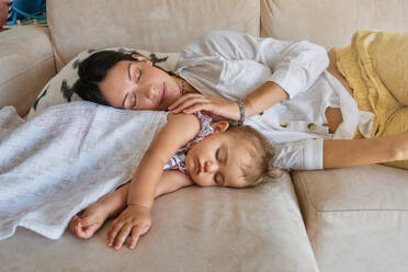 Young mother with adorable baby sleeping together on comfortable sofa in living room at home - ADSF46745