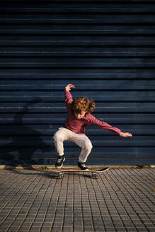 Ganzkörper energischer Junge in Freizeitkleidung macht Trick auf dem Skateboard auf dem Bürgersteig gegen dunkelblaue Wand am Wochenende in der Stadt Straße - ADSF46783