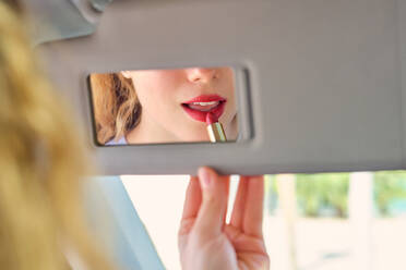 Crop weiblichen Fahrer Anwendung leuchtend roten Lippenstift und Blick in Kosmetikspiegel auf Sonnenblende, während im Auto sitzen bei sonnigem Wetter - ADSF46784