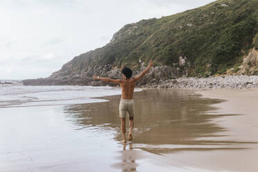 Man with arms outstretched walking at beach - PBTF00246