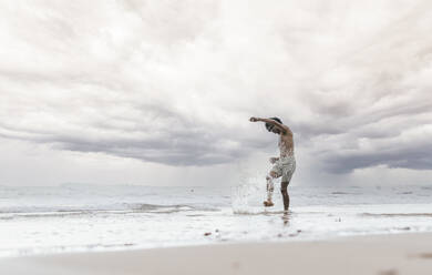 Mann spritzt Wasser am Strand unter Himmel - PBTF00248