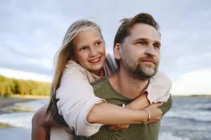 Lächelnder Vater, der seine Tochter am Strand huckepack nimmt - EYAF02820