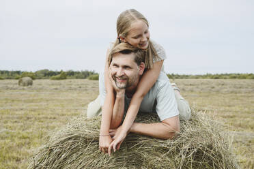 Happy daughter and father lying on hay in field - EYAF02824