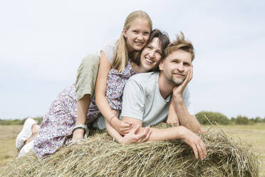 Happy daughter with father and mother lying on hay in field - EYAF02827