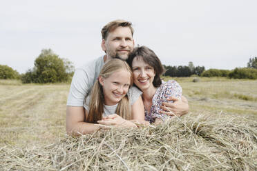 Happy family leaning on hay in field - EYAF02834