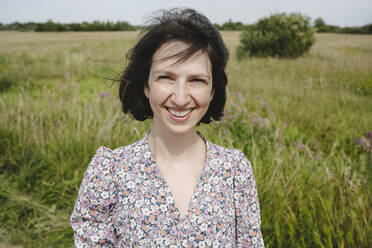 Smiling woman standing in front of grass on sunny day at field - EYAF02837