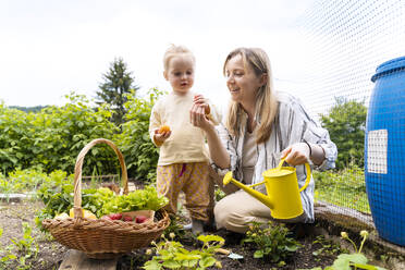 Lächelndes Mädchen mit Mutter bei der Gartenarbeit und dem Pflücken von Erdbeeren - NDEF01130