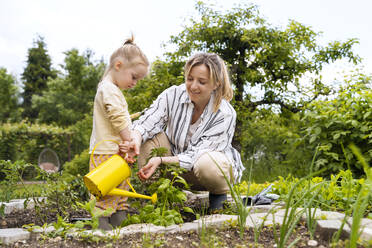 Glückliche Mutter und Tochter gießen Pflanzen mit einer Gießkanne im Garten - NDEF01134