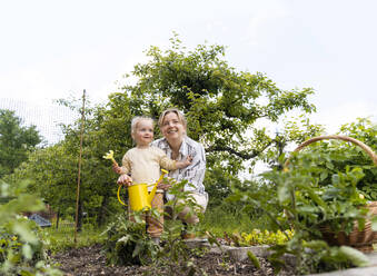 Glückliche Mutter und Tochter mit Gießkanne im Garten - NDEF01136