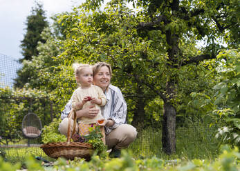Happy mother and daughter with basket of fresh vegetables in garden - NDEF01138