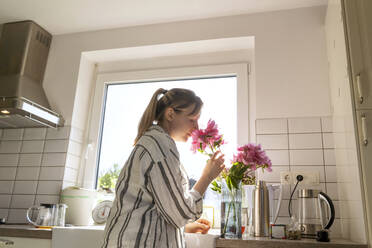 Frau riecht frische rosa Blumen in der Küche zu Hause - NDEF01148