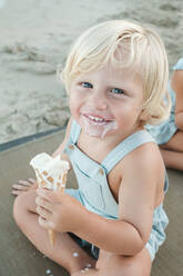 Hoher Winkel des fröhlichen kleinen Jungen mit Eis lächelnd und Blick auf die Kamera, während am Strand ausruhen - ADSF46865