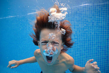 Verrückter Junge schreit mit geöffnetem Mund beim Schwimmen im blauen Wasser des Pools - ADSF46874