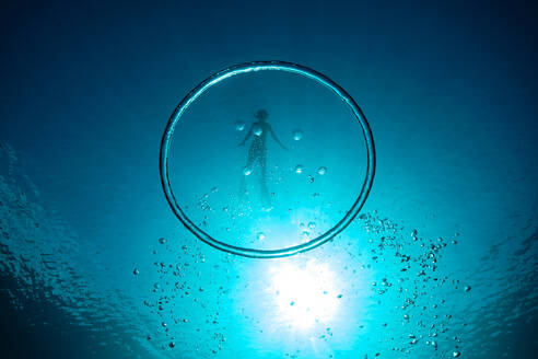 Underwater shot of big bubble ring against unrecognizable boy diving in deep blue ocean during vacation - ADSF46878