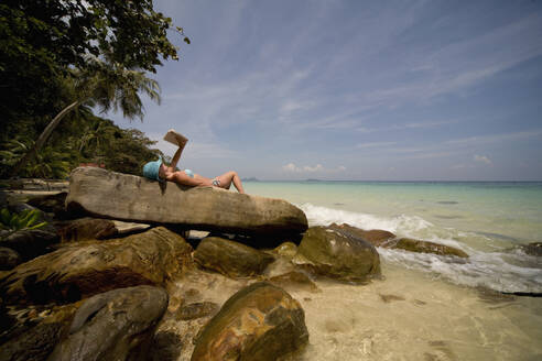 Rücken einer jungen Frau, die auf den Felsen liegt und sich sonnt und entspannt, Koh Phi Phi, Thailand - FSIF06377