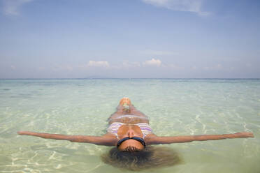 Young woman floating in crystal clear sea water with arms wide open, Koh Phi Phi, Thailand - FSIF06378