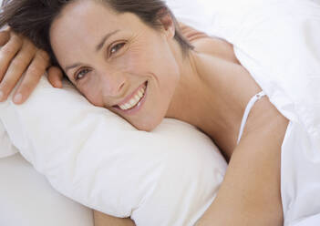 Lächelnde Frau liegt im Bett und umarmt ein Kissen - FSIF06390
