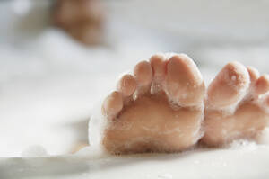 Nahaufnahme einer Frau, deren Füße mit Schaum bedeckt sind und die aus einer Badewanne steigt - FSIF06403