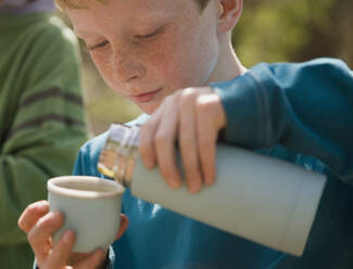 Nahaufnahme eines Jungen, der Wasser aus einer Isolierflasche einschenkt - FSIF06545