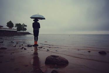 Woman with an umbrella by the sea wind rain - INGF12079