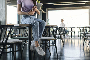 Tiefschnitt einer jungen Frau, die mit einem Laptop in der Hand auf einem Cafétisch sitzt - ASGF04549