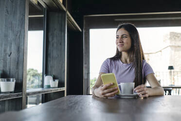 Portrait of pretty brunette sitting at office table with smart phone in hand - ASGF04555