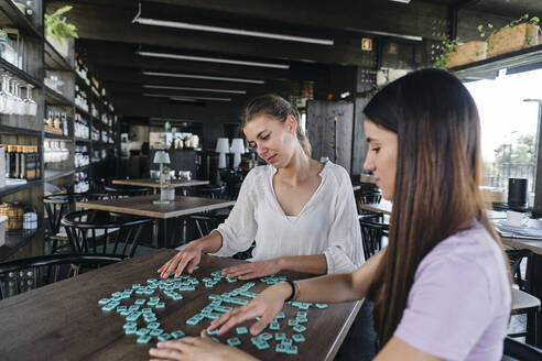 Zwei junge Frauen spielen ein Wortspiel an einem Kaffeetisch - ASGF04621