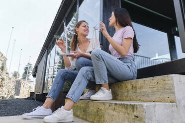 Two female engineers talking outdoors with models of wind turbines in hands - ASGF04622