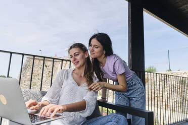 Zwei junge Frauen benutzen einen Laptop auf einem Balkon - ASGF04628
