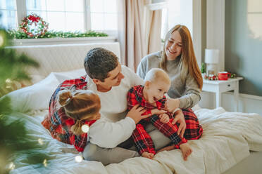 Familie sitzt auf dem Bett und feiert Weihnachten zu Hause - NLAF00105