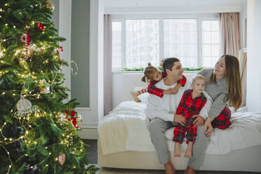 Familie sitzt auf dem Bett in der Nähe des Weihnachtsbaums zu Hause - NLAF00127