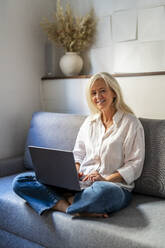 Smiling mature freelancer sitting with laptop - DLTSF03626