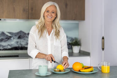 Lächelnde Frau, die Obst schneidet und das Frühstück zu Hause zubereitet - DLTSF03630
