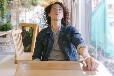 Young man looking up and sitting at table in cafe - DSIF00680