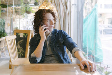 Smiling young man talking on smart phone in cafe - DSIF00681