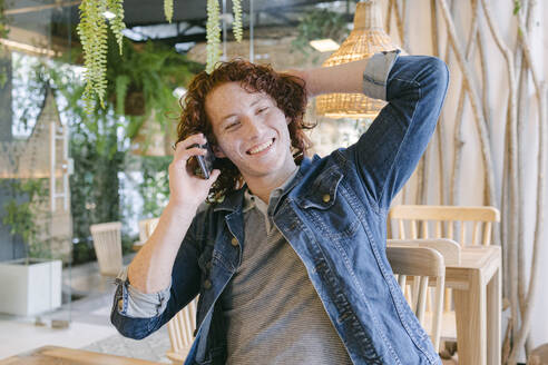 Happy young man talking on mobile phone in cafe - DSIF00683