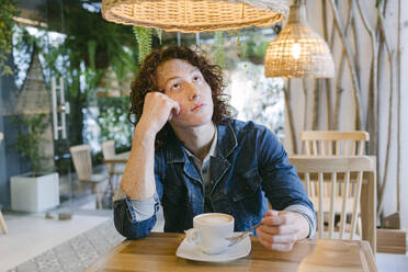 Nachdenklicher junger Mann sitzt mit einer Kaffeetasse am Tisch in einem Cafe - DSIF00689