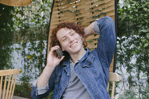 Happy young man sitting and talking on smart phone in cafe - DSIF00695