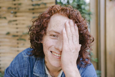 Happy redhead man covering face with hand in cafe - DSIF00698