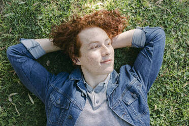 Thoughtful young man with hands behind head relaxing on grass - DSIF00704