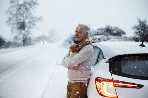 Contemplative man leaning on car in snow - JOSEF21016