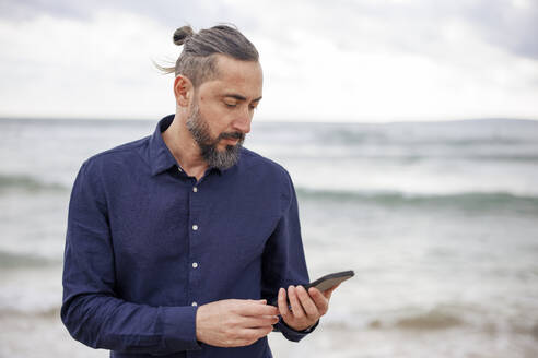 Älterer Mann benutzt Smartphone am Strand - JOSEF21027