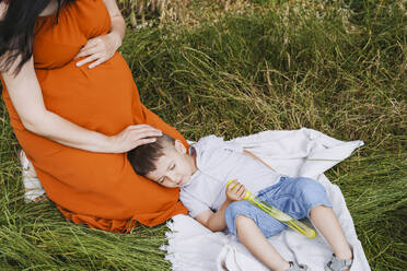 Schwangere Mutter streichelt schlafenden Sohn im Gras - NDEF01152