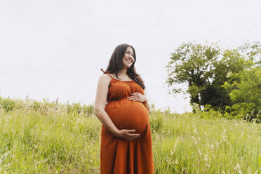 Glückliche schwangere Frau im Gras stehend - NDEF01155