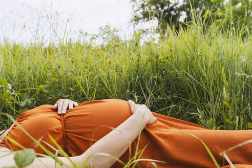 Pregnant woman lying near grass in meadow - NDEF01171