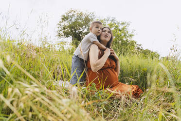 Sohn umarmt schwangere Mutter im Grasbereich - NDEF01176