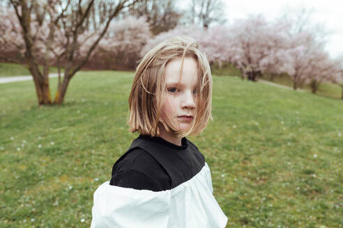 Von oben Porträt von ernsten preteen Mädchen mit kurzen Haaren stehen im Park in der Nähe blühenden Kirschen - ADSF46976