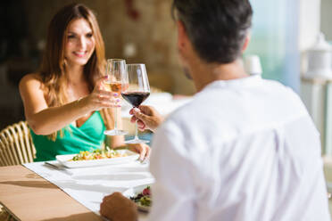 Verliebtes Paar in eleganter Kleidung schaut sich an und lächelt, während es am Tisch mit Salaten sitzt und gemeinsam einen Toast ausspricht, während eines Dates - ADSF46981